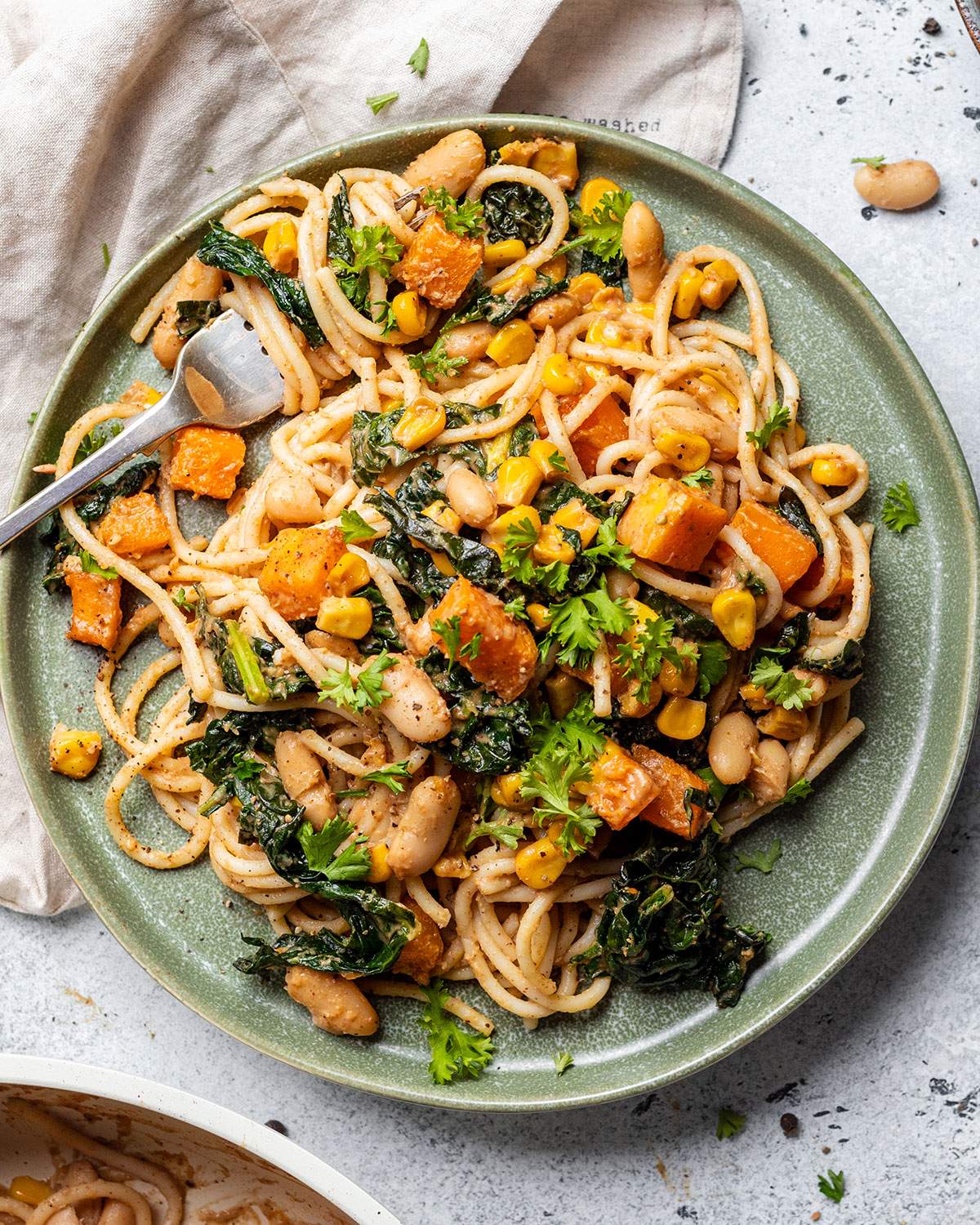 A plate filled with vegan satay pasta and vegetables, with a fork on the side.