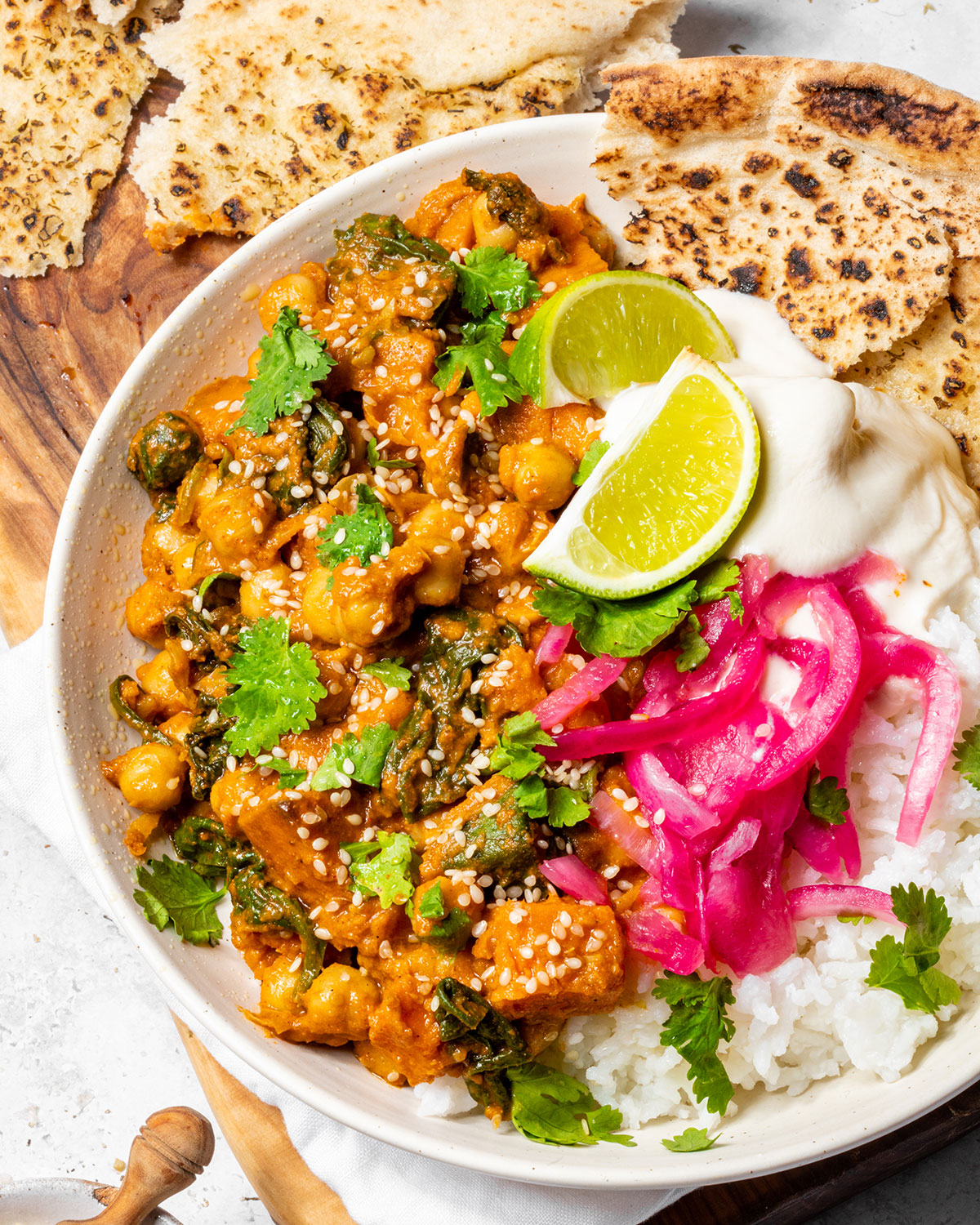 A bowl of chickpea curry with sweet potato on a serving board.