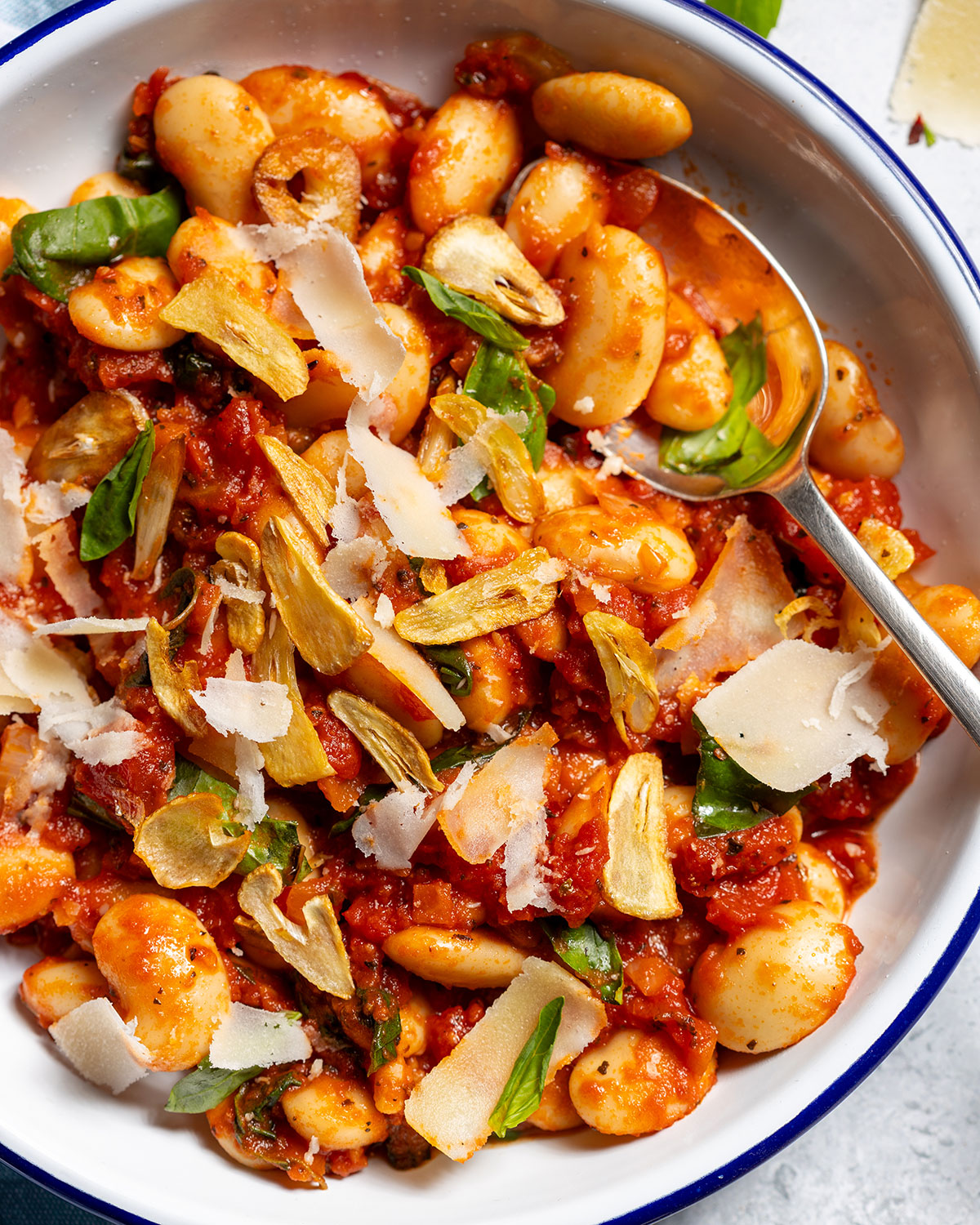 A plate of butter beans in a spicy tomato sauce with a spoon on the side.