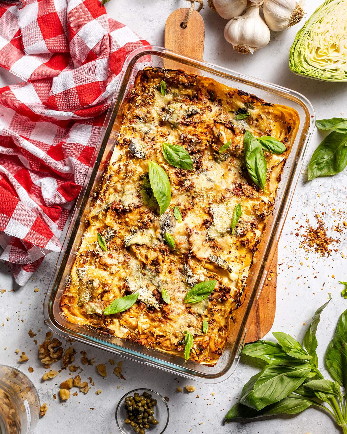 Freshly baked vegan cabbage lasagna in an oven dish surrounded by ingredients.