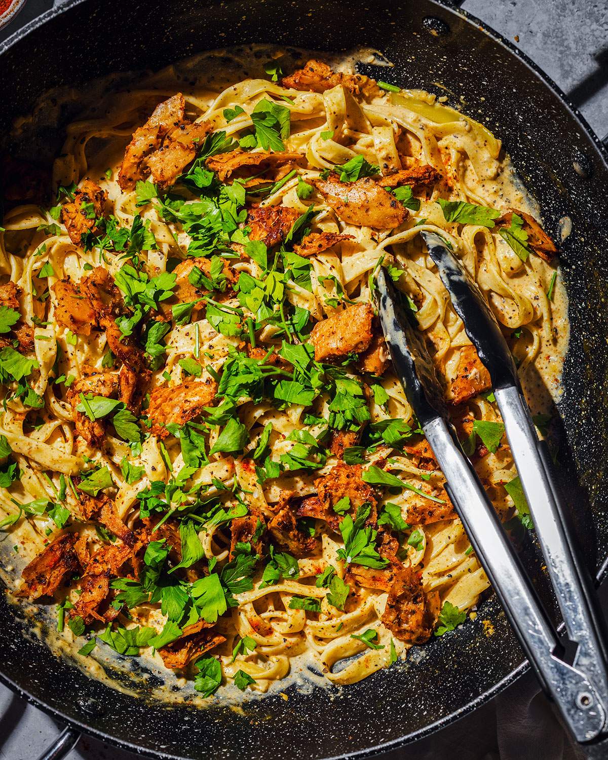Creamy cajun alfredo with vegan cajun chicken pieces in a skillet.