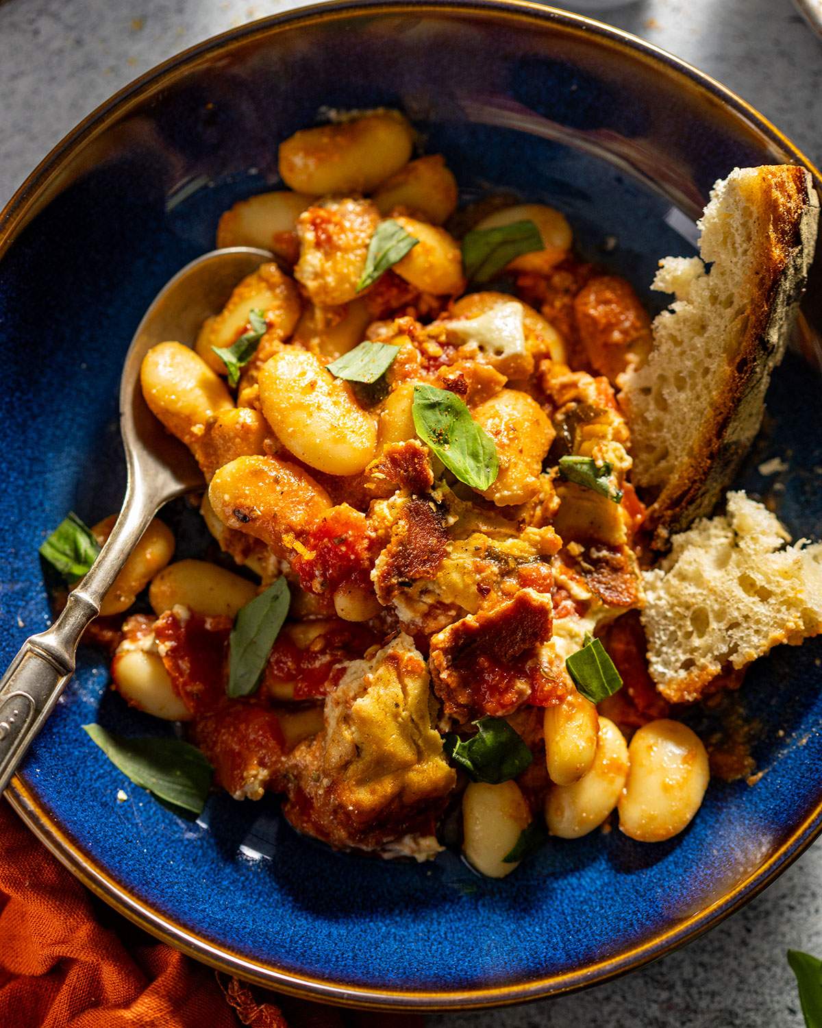Baked butter beans served in a bowl with crusty bread and a spoon on the side.
