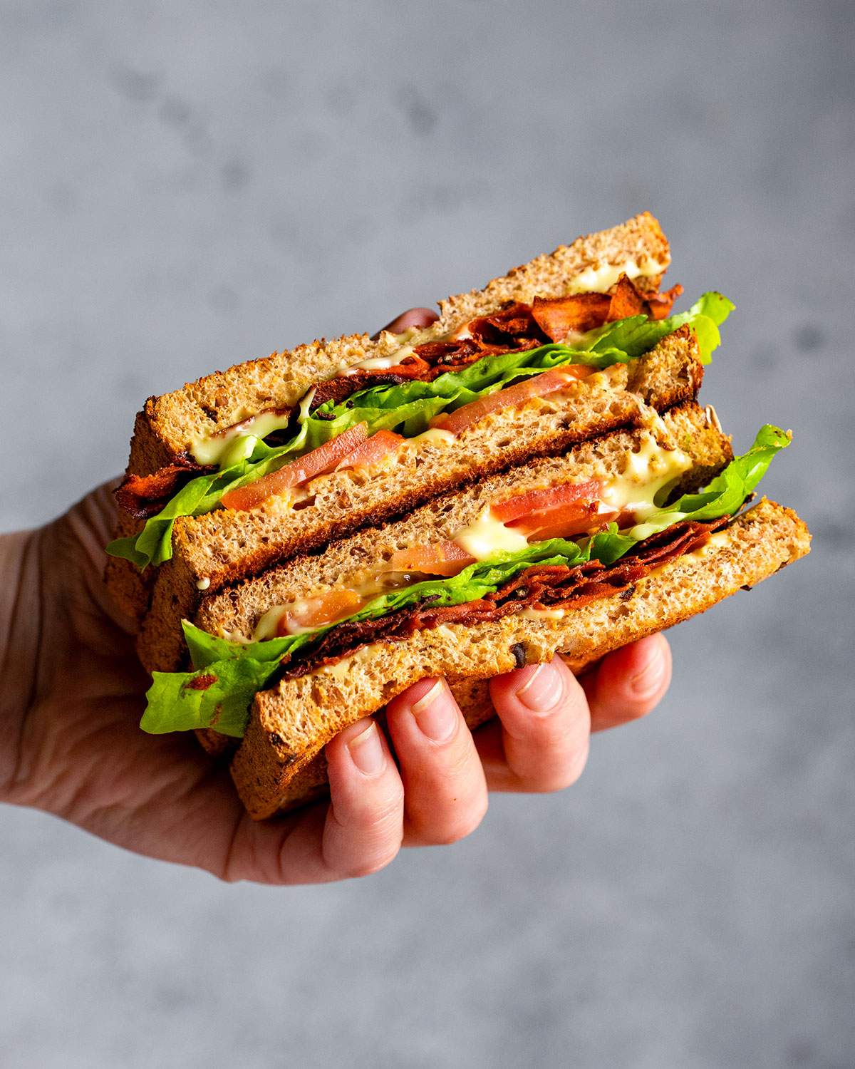 A hand holding a vegan BLT sandwich with carrot bacon.