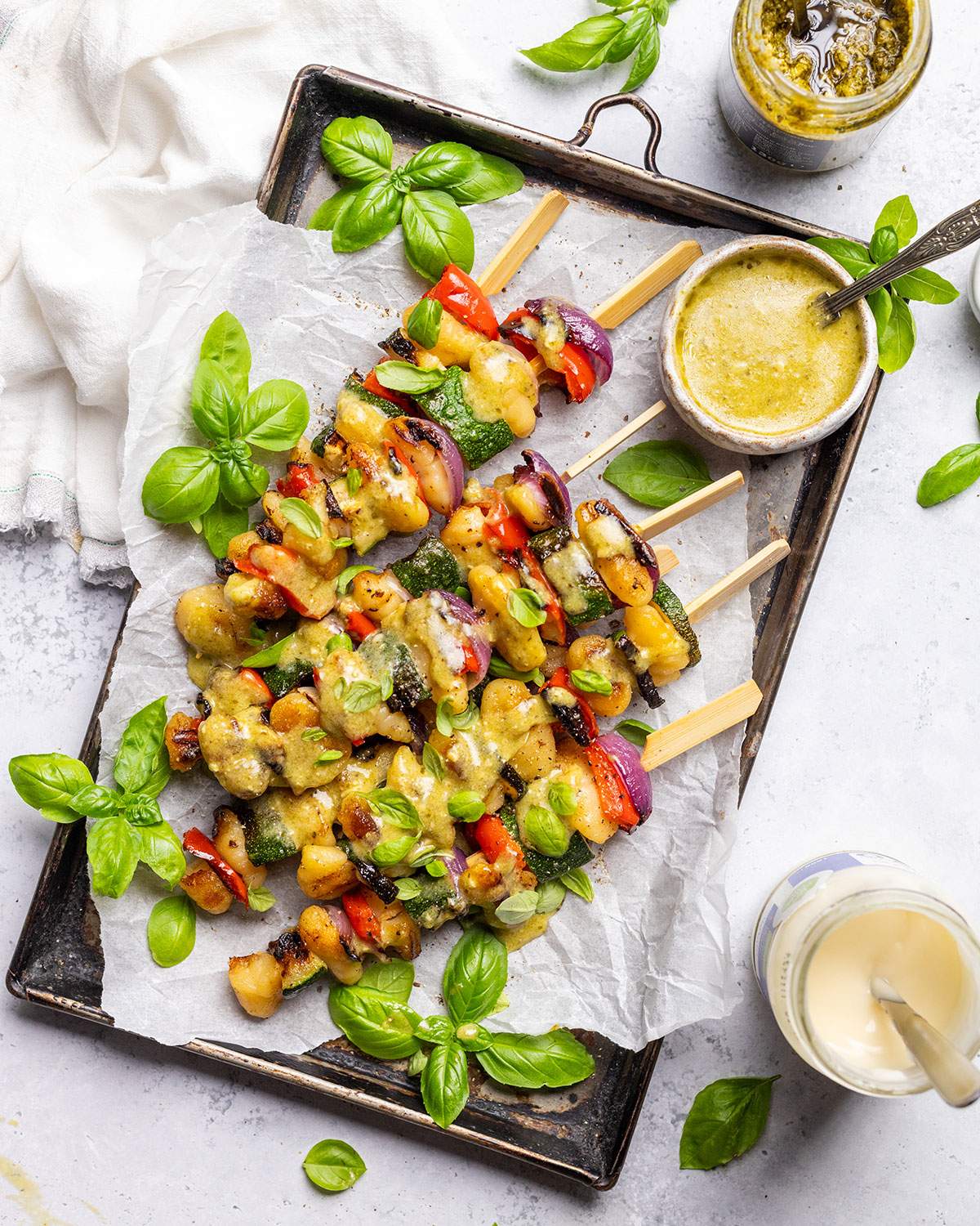 Vegan skewers with gnocchi and vegetables on a platter with pesto drizzle.