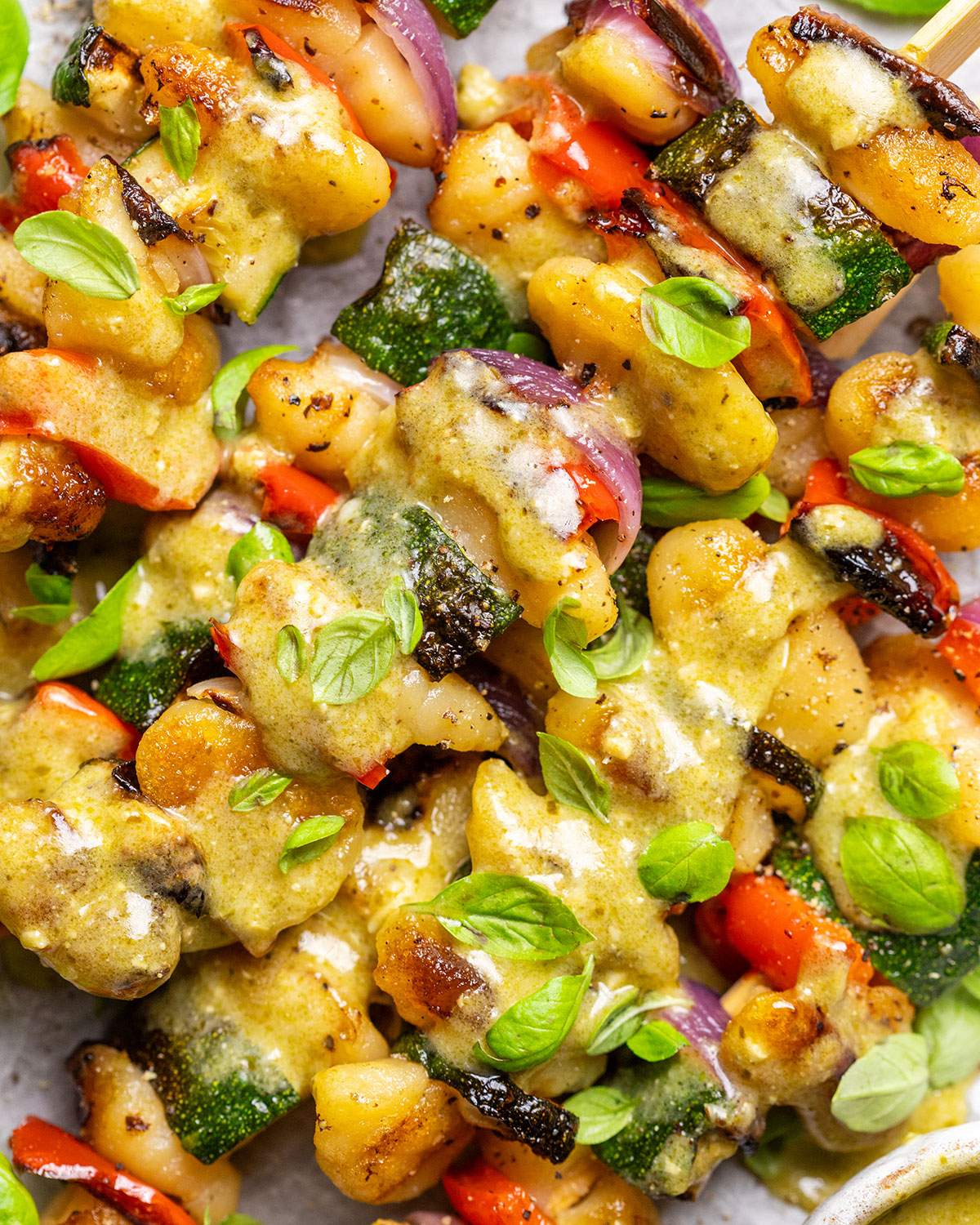Vegan skewers with gnocchi and vegetables and pesto drizzle.