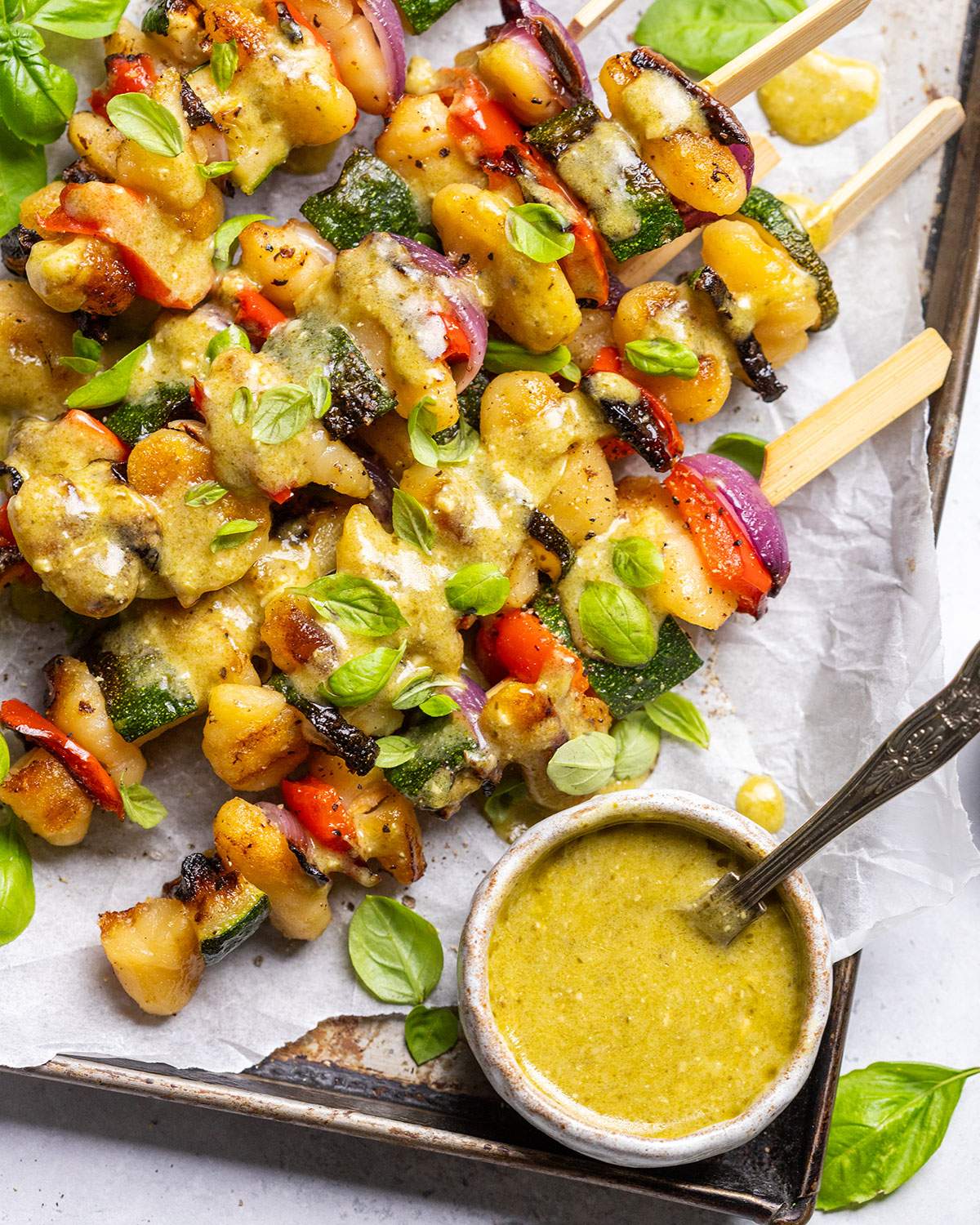 Vegan skewers with gnocchi and vegetables on a platter with pesto drizzle.