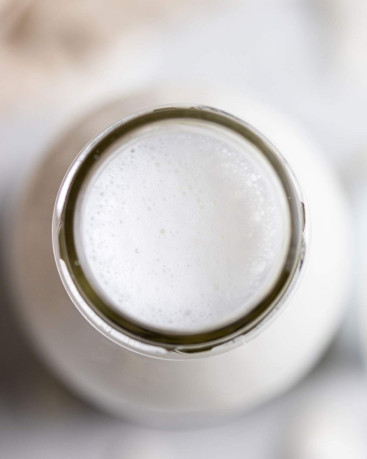 Frothy coconut milk in a glass bottle seen from above.
