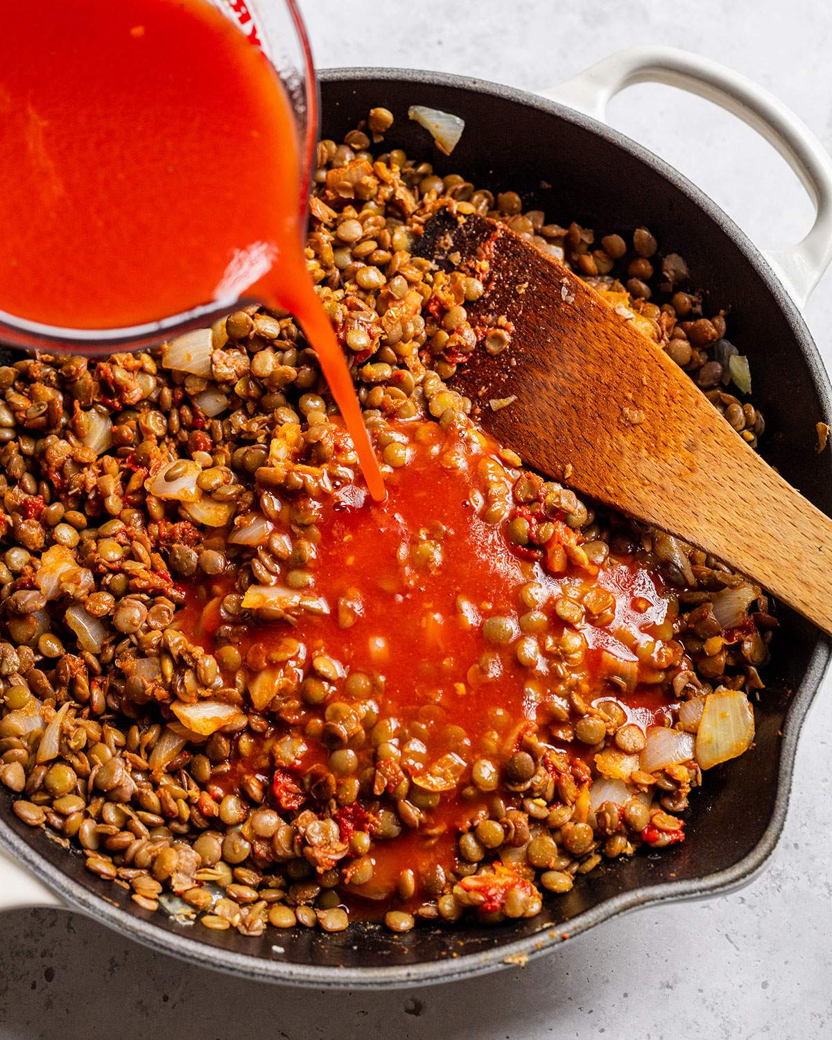 Pouring tomato sauce into lentils in a skillet.