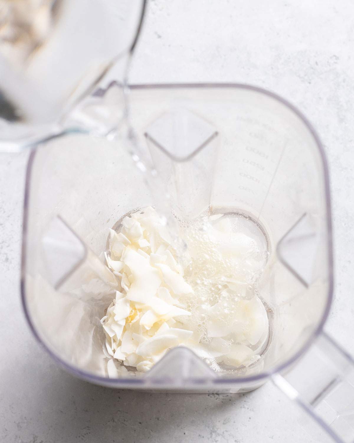 Pouring water onto coconut flakes in a blender.