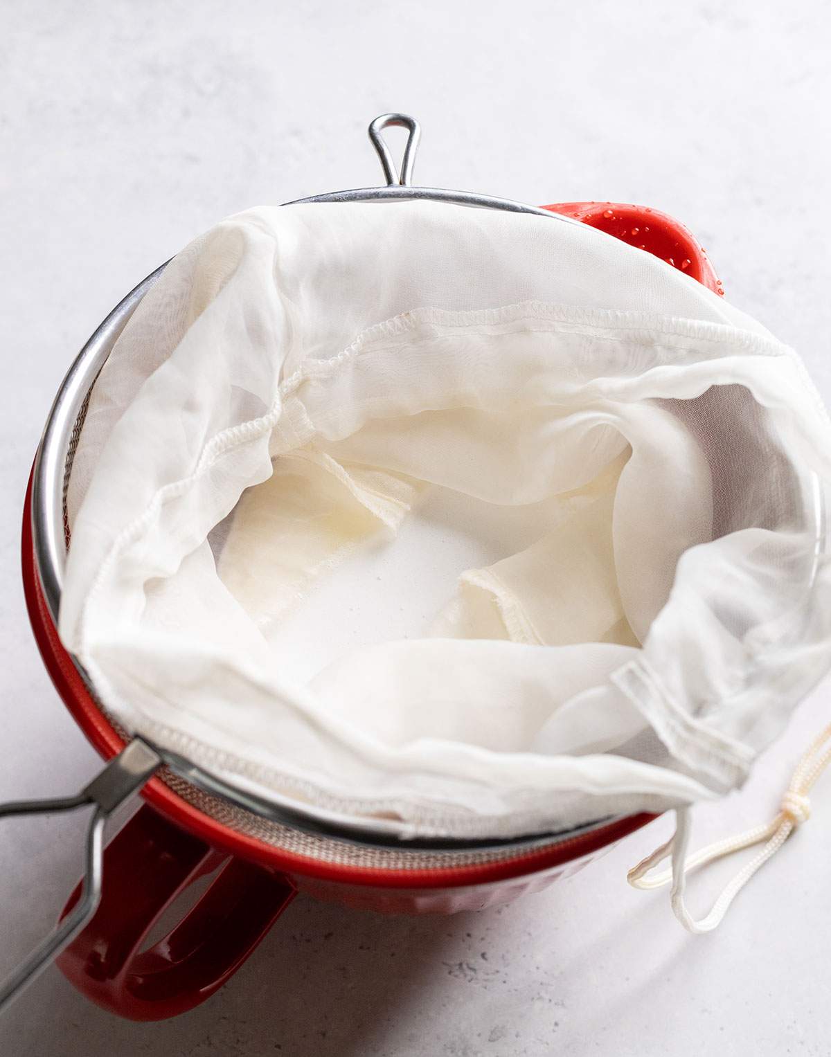 Straining coconut milk through a nut milk bag above a bowl.