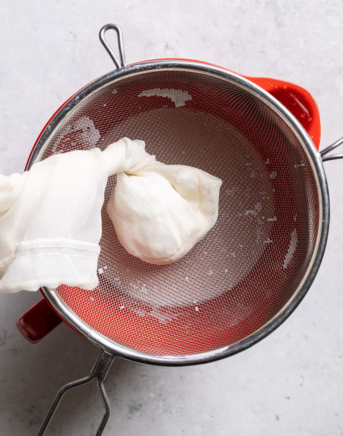 Squeezed nut milk bag in a sieve over a bowl.