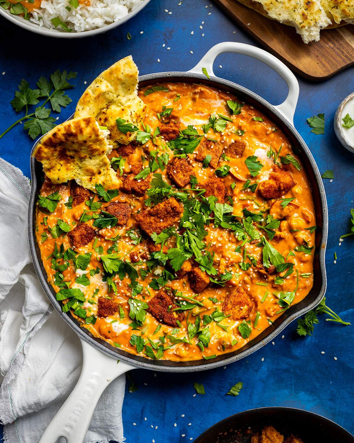 A skillet filled with vegan butter chickpea curry with tofu and naan bread.