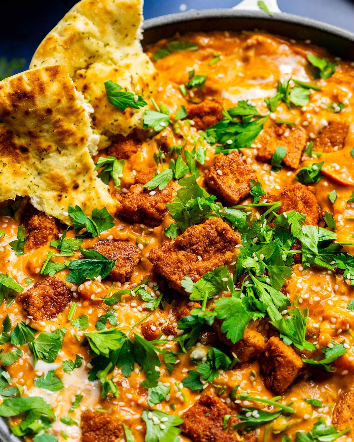 Vegan chickpea curry in a skillet with naan bread on the side.
