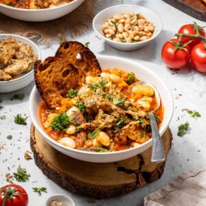 A bowl filled with hearty tomato and butter bean stew surrounded by ingredients.