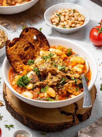 A bowl filled with hearty tomato and butter bean stew surrounded by ingredients.