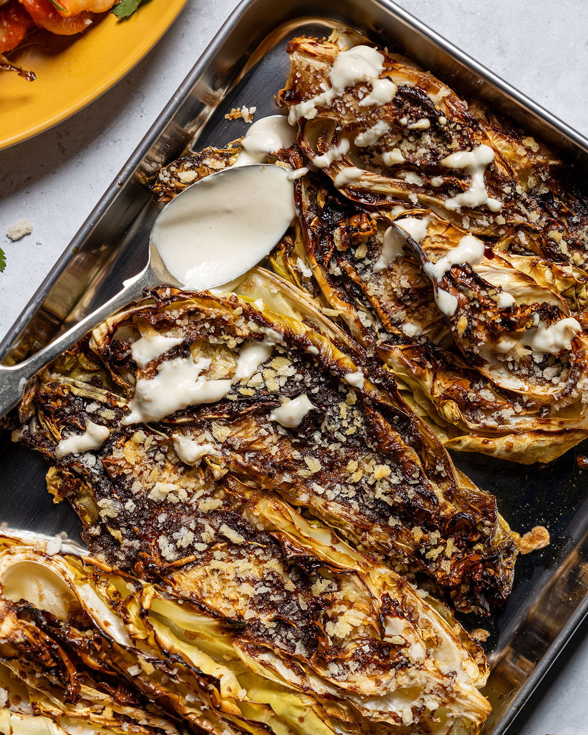 Baked Cabbage steaks topped with yogurt drizzle on a oven tray.