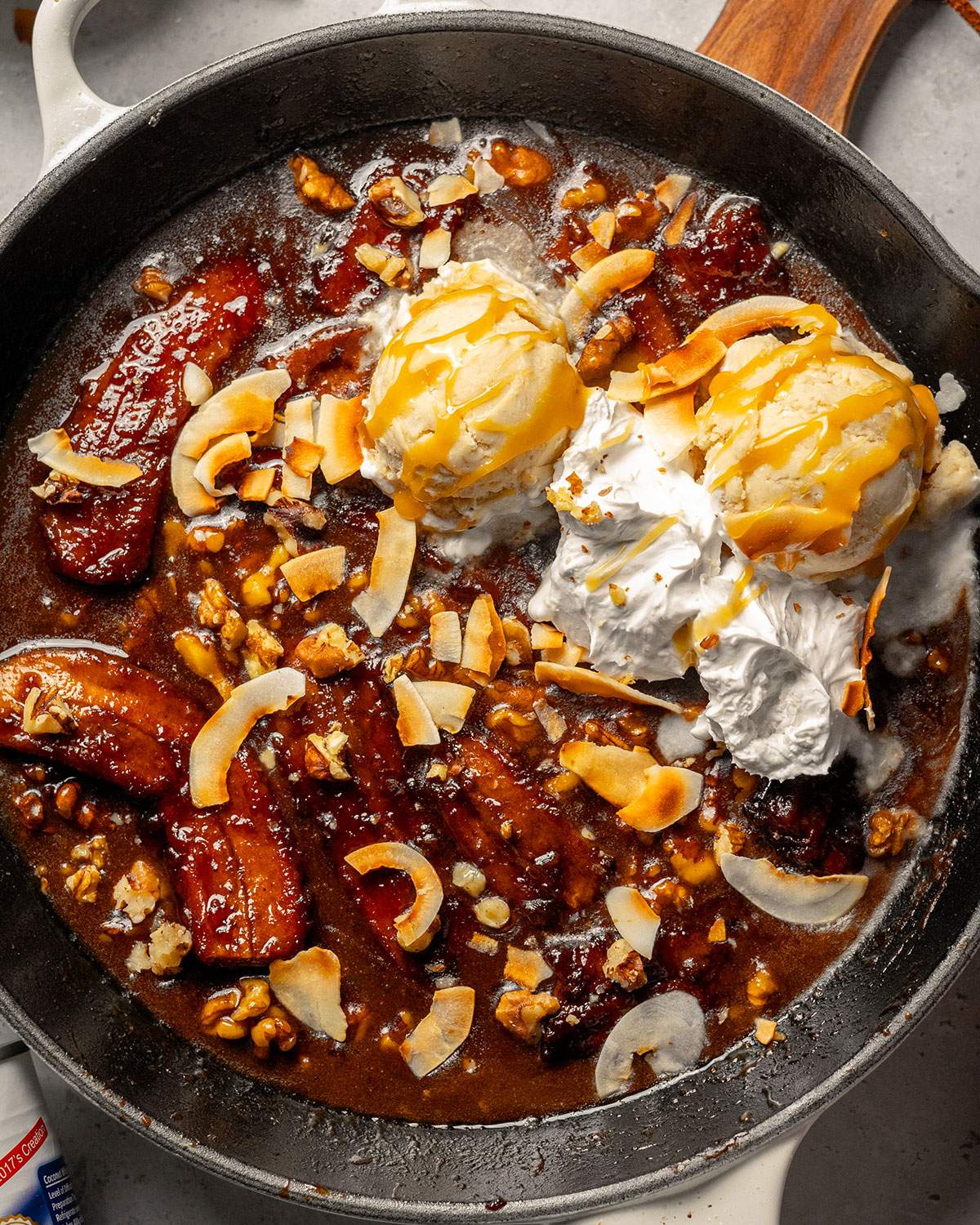 A skillet filled with homemade vegan bananas foster with 2 balls of vanilla ice cream on top.