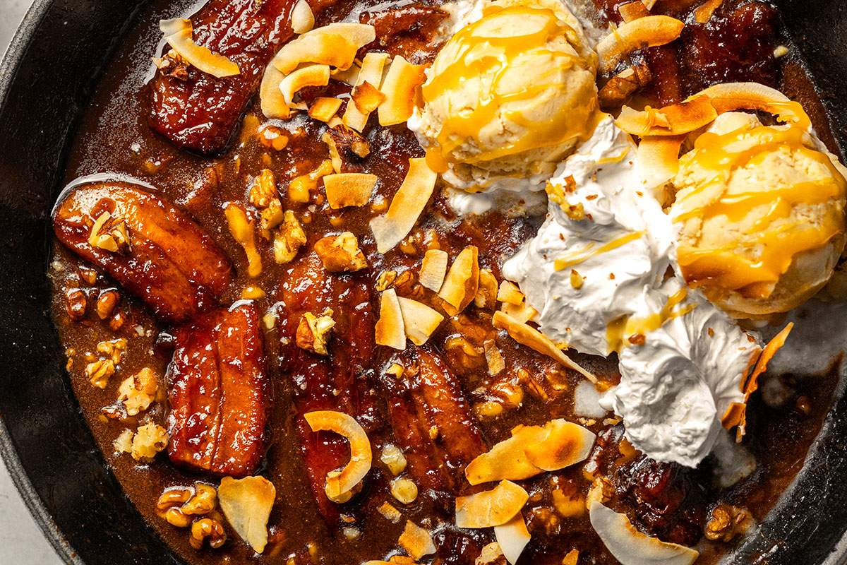 Vegan Bananas Foster shown up close in a skillet, with ice cream and whipped cream.