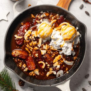 A skillet filled with vegan bananas foster served with vanilla ice cream and whipped coconut cream.