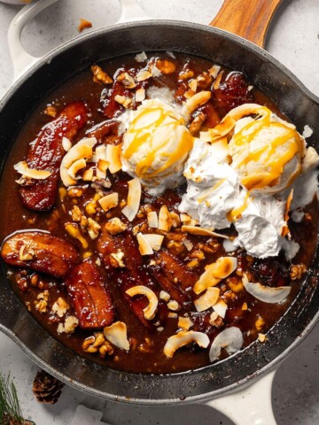 A skillet filled with vegan bananas foster served with vanilla ice cream and whipped coconut cream.
