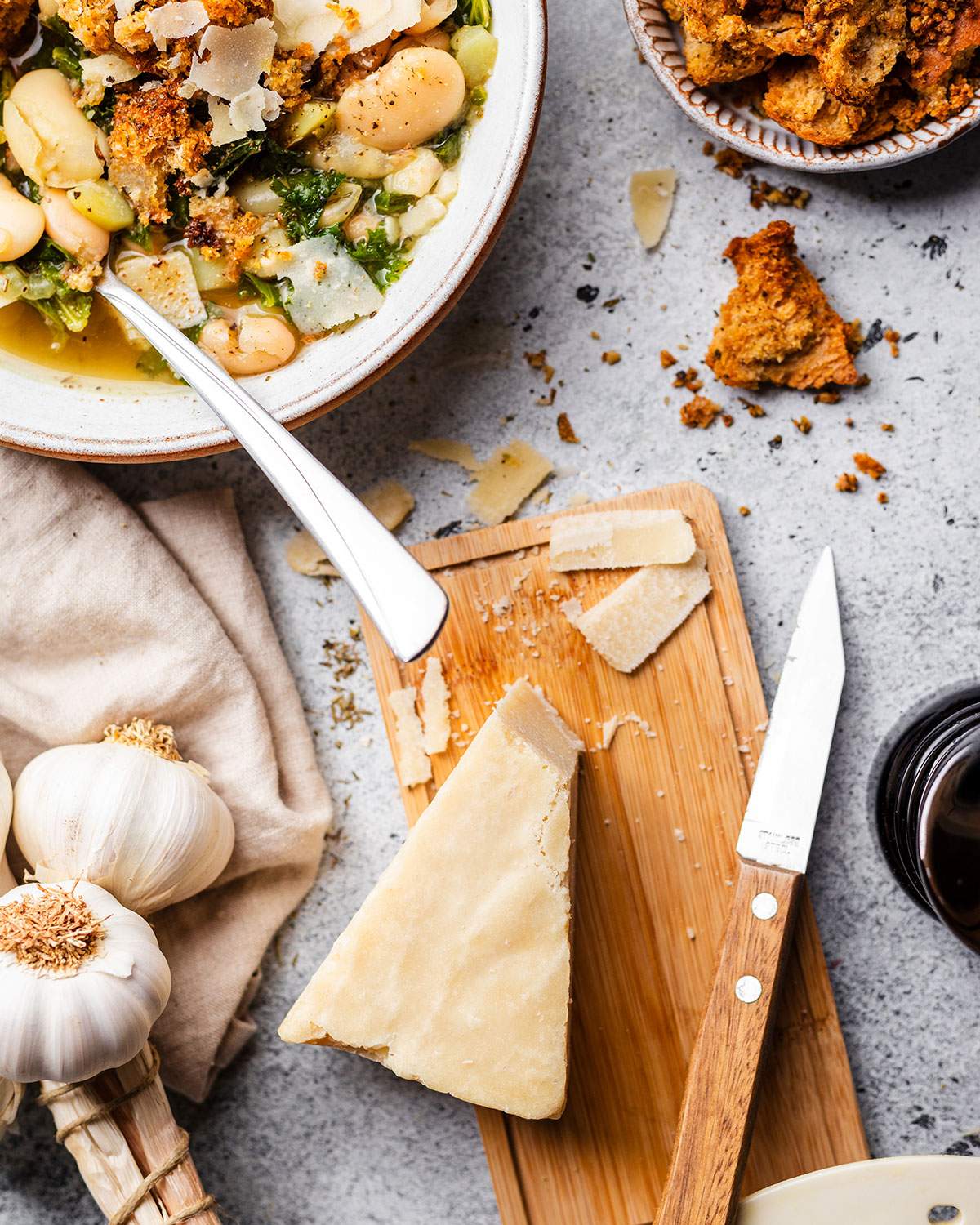 A block of vegan parmesan next to a knife on the dinner table, alongside a bowl of soup.
