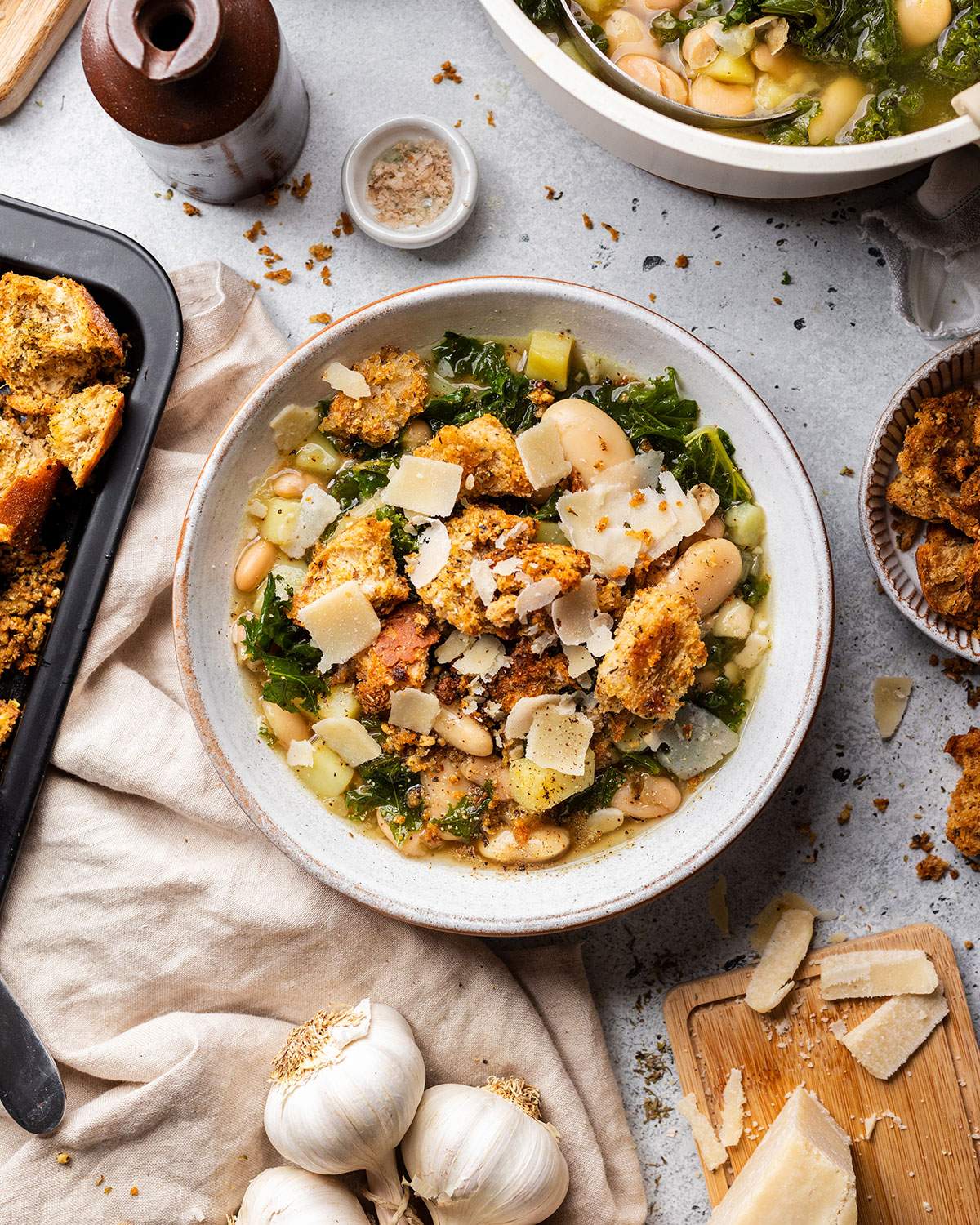 A bowl full of rustic butter bean and kale soup with kale, homemade chunky croutons on the dinner table.