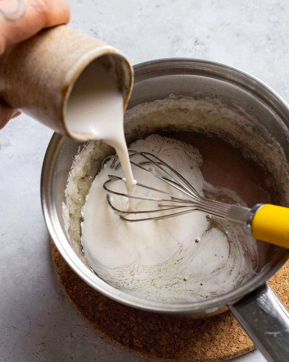 Pouring vegan cream into sugar mix in a saucepan.