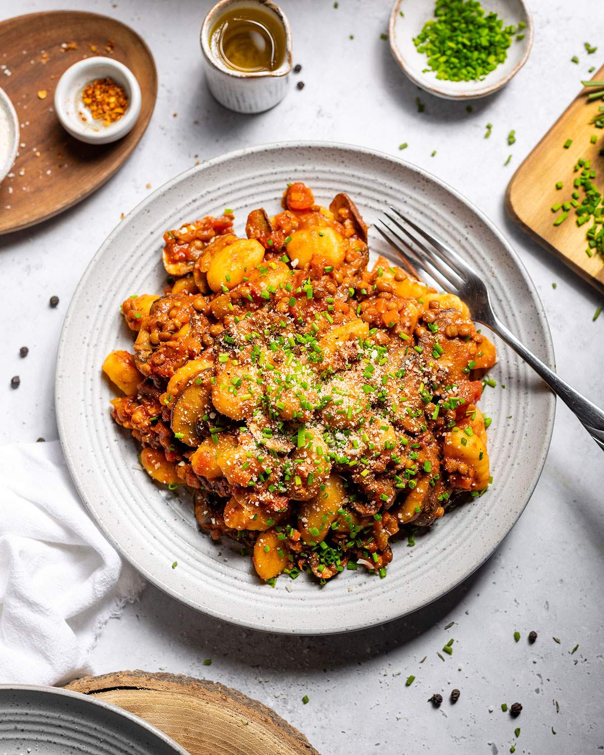 Vegan gnocchi with hearty lentil ragu and fresh chives on a serving plate on the dinner table.