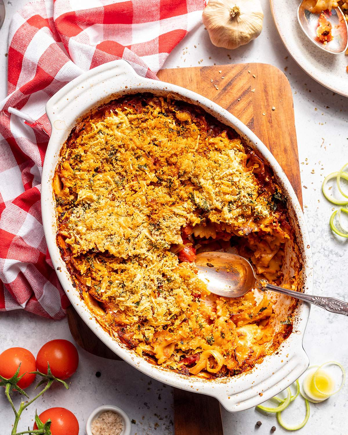 A casserole dish filled with vegan pasta bake and a serving spoon on the side.
