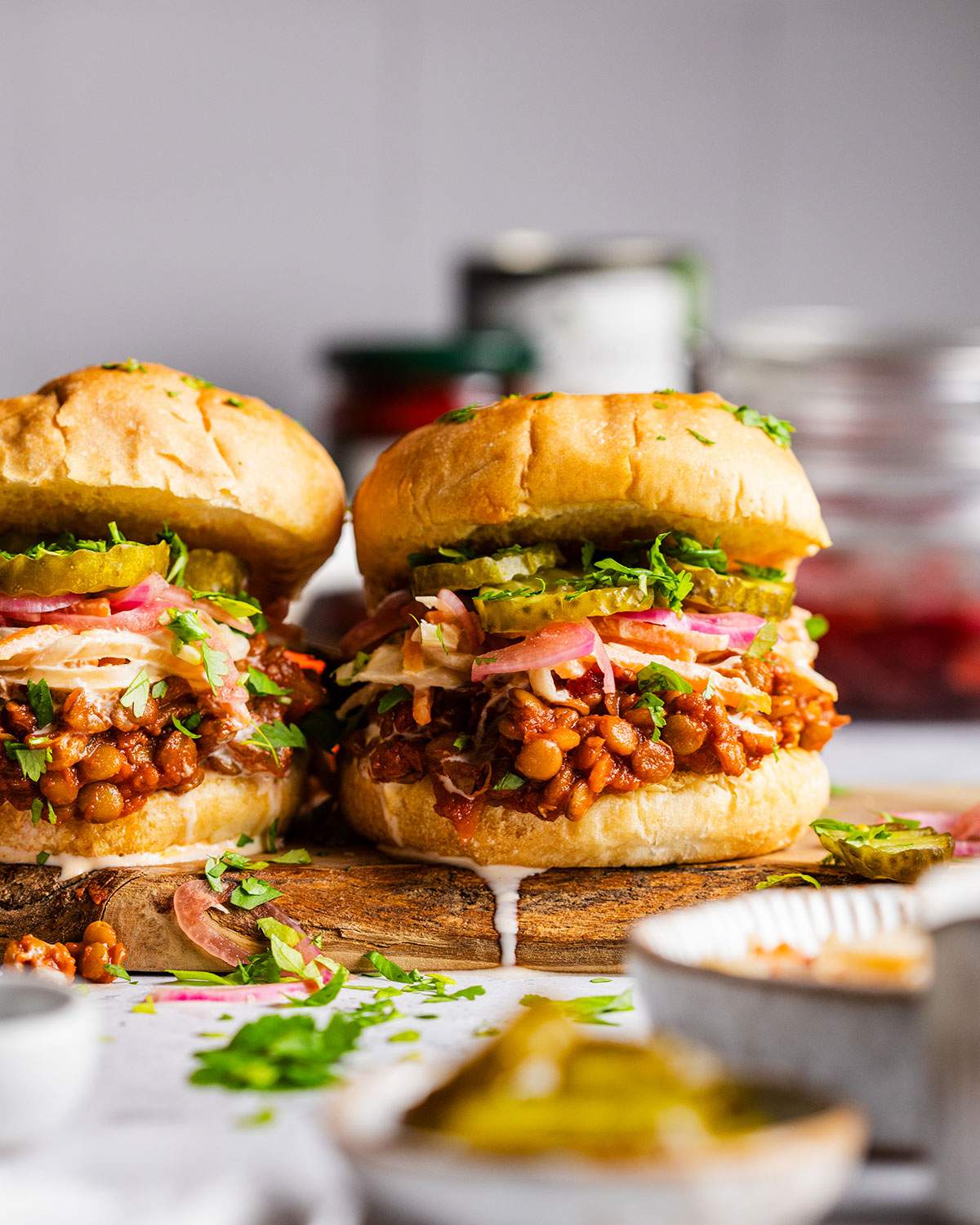 Two Vegan sloppy joes on a serving board with lentils and pickles.