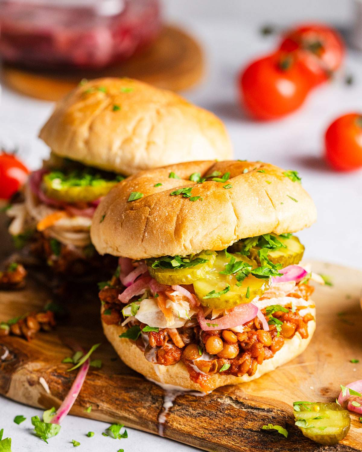 Two Vegan sloppy joes on a serving board with lentils and pickles.