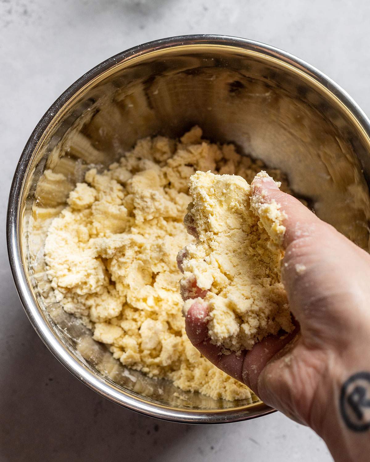 A hand mixing vegan shortcrust pastry dough in a mixing bowl.