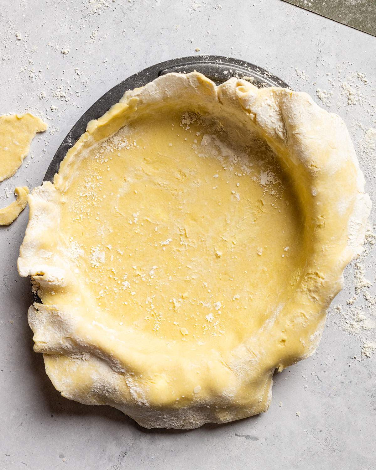 Vegan pastry dough in a tart tin before cutting off excess dough.