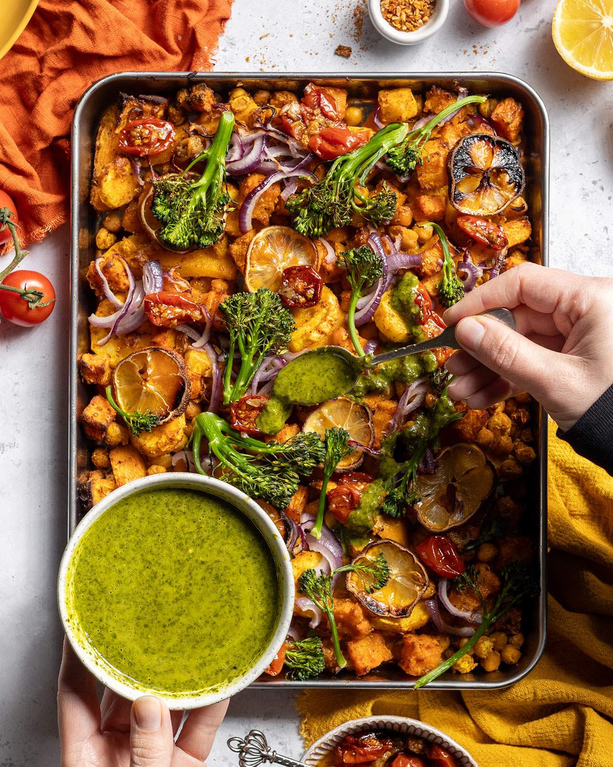 Spooning a herby sauce over a roasted vegetable and chickpea traybake.