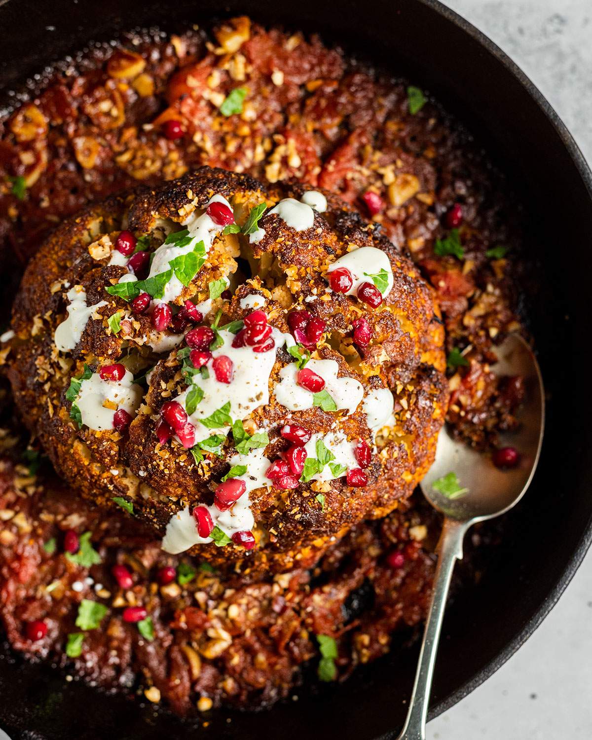 A skillet with a whole roasted cauliflower in a spicy tomato sauce.