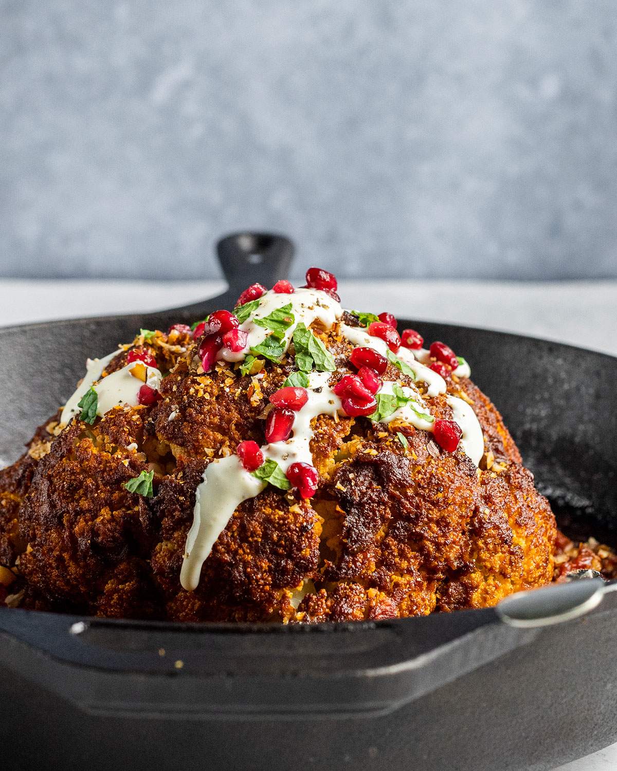 Roasted cauliflower with a seasoning crust in a skillet, with yogurt drizzle and pomegranate seeds.