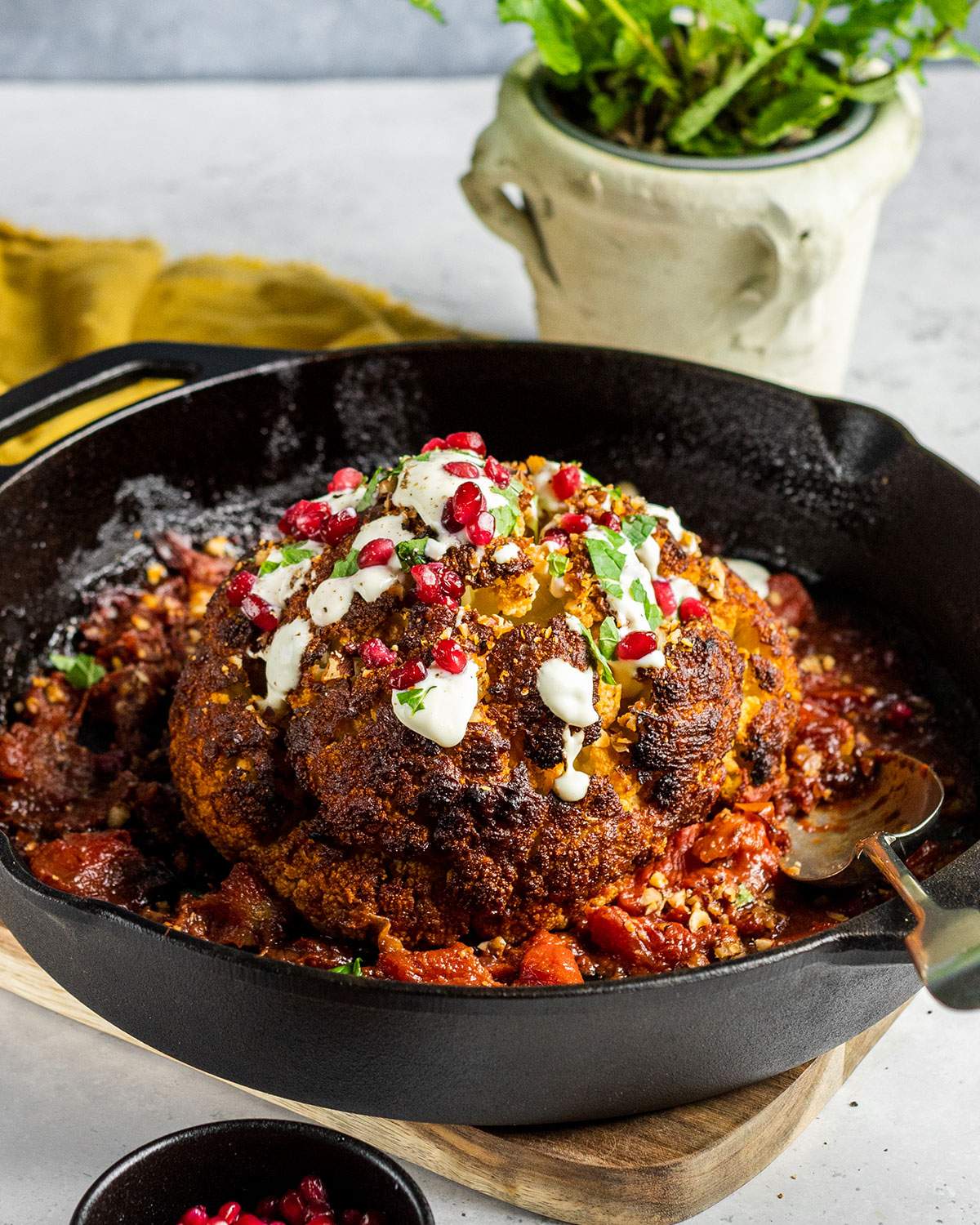 A whole roasted cauliflower in a cast iron skillet garnished with fresh pomegranate seeds.