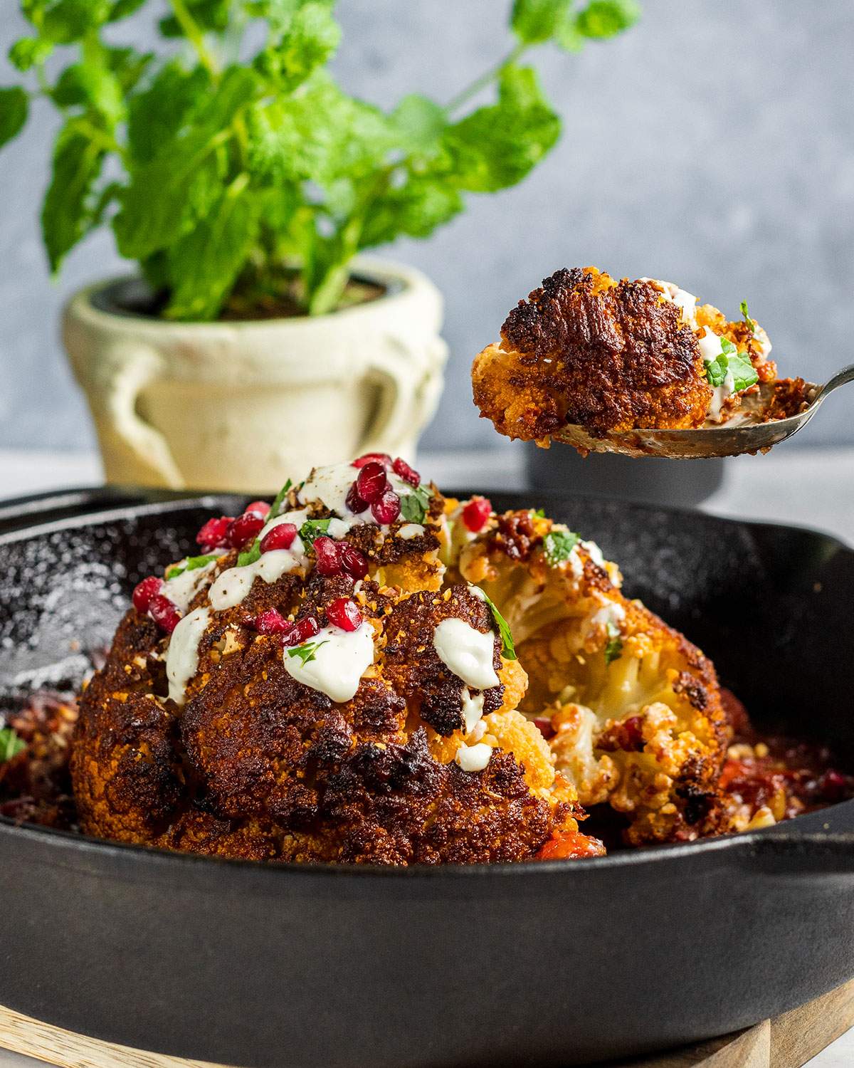 Whole roasted cauliflower in a cast iron skillet and a serving spoon lifting a piece.