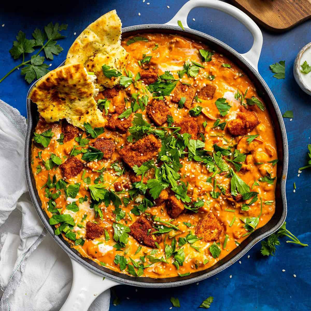 A skillet filled with creamy chickpea curry with tofu on top.