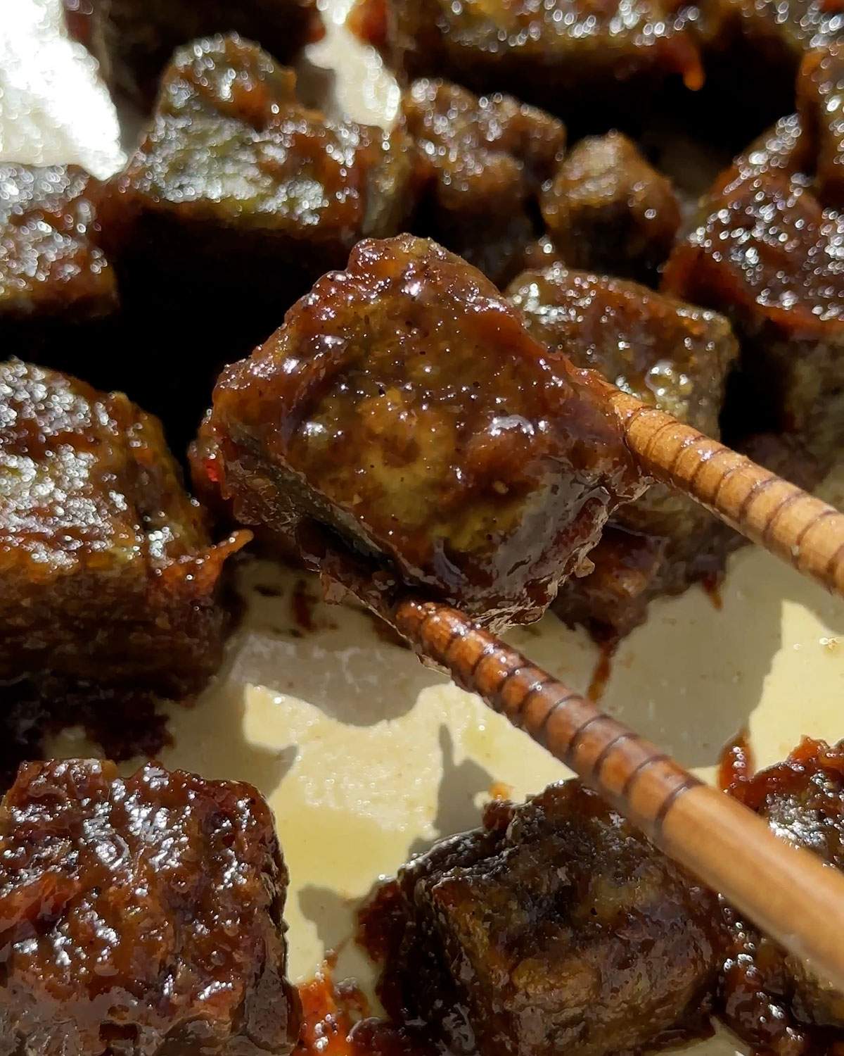 Chopsticks picking up a cube of pumpkin tofu coated in sauce.