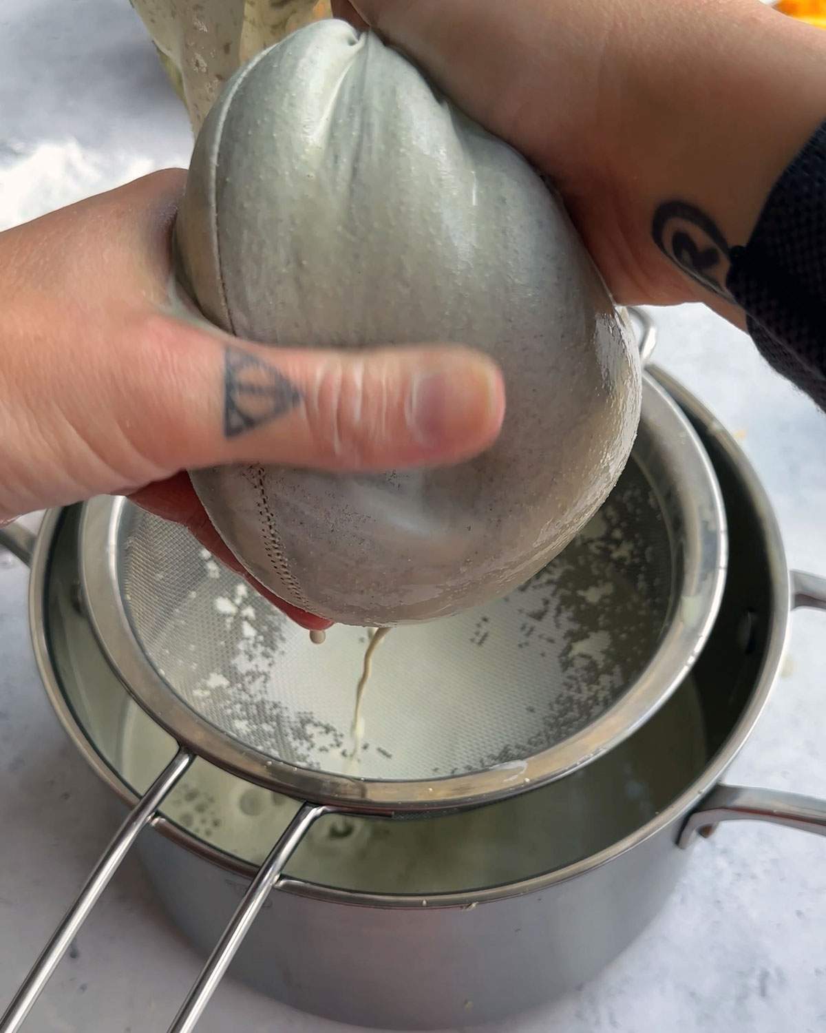 Hands squeezing pumpkin seed milk from a full nut milk bag.