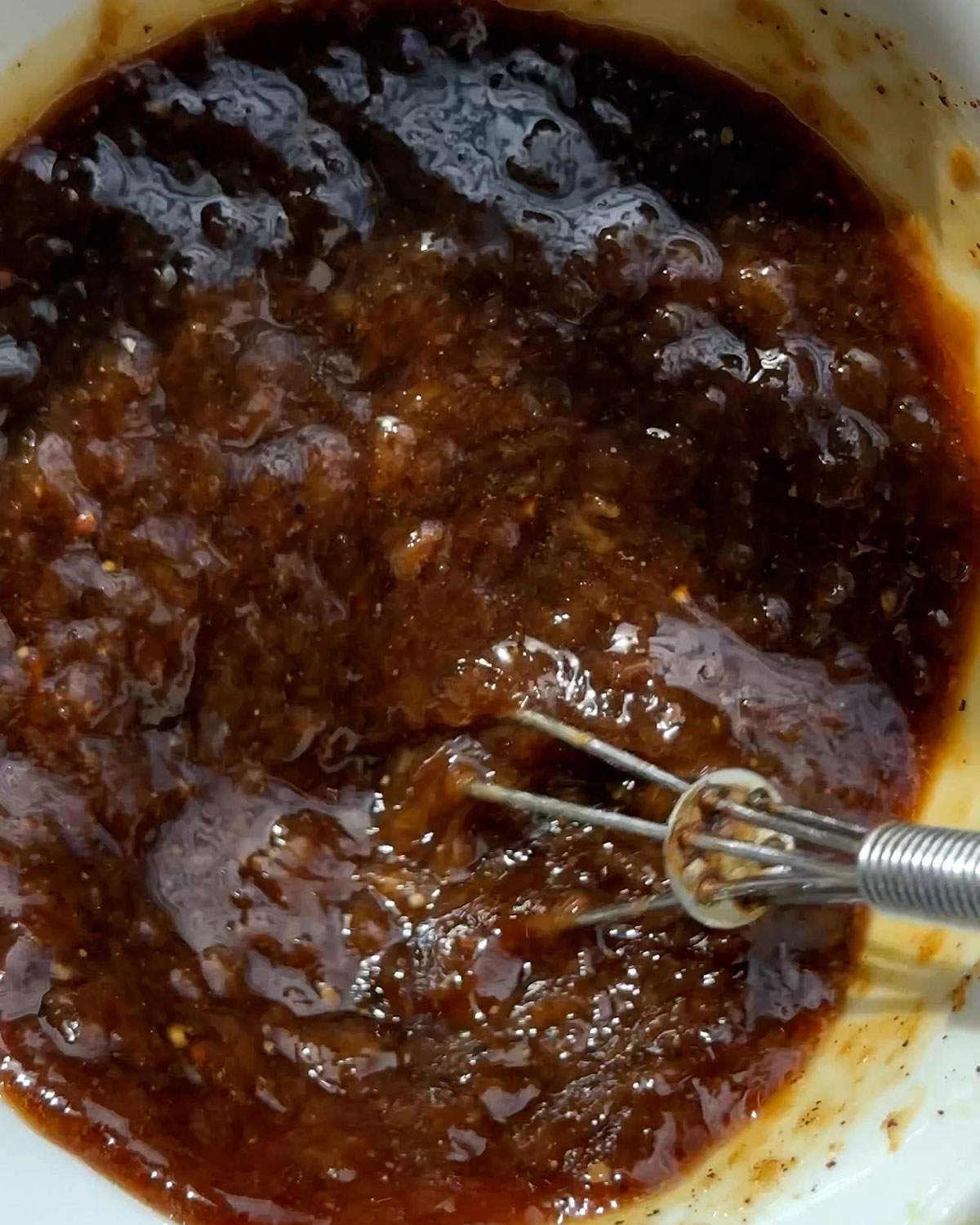 Whisking black pepper sauce in a small bowl.