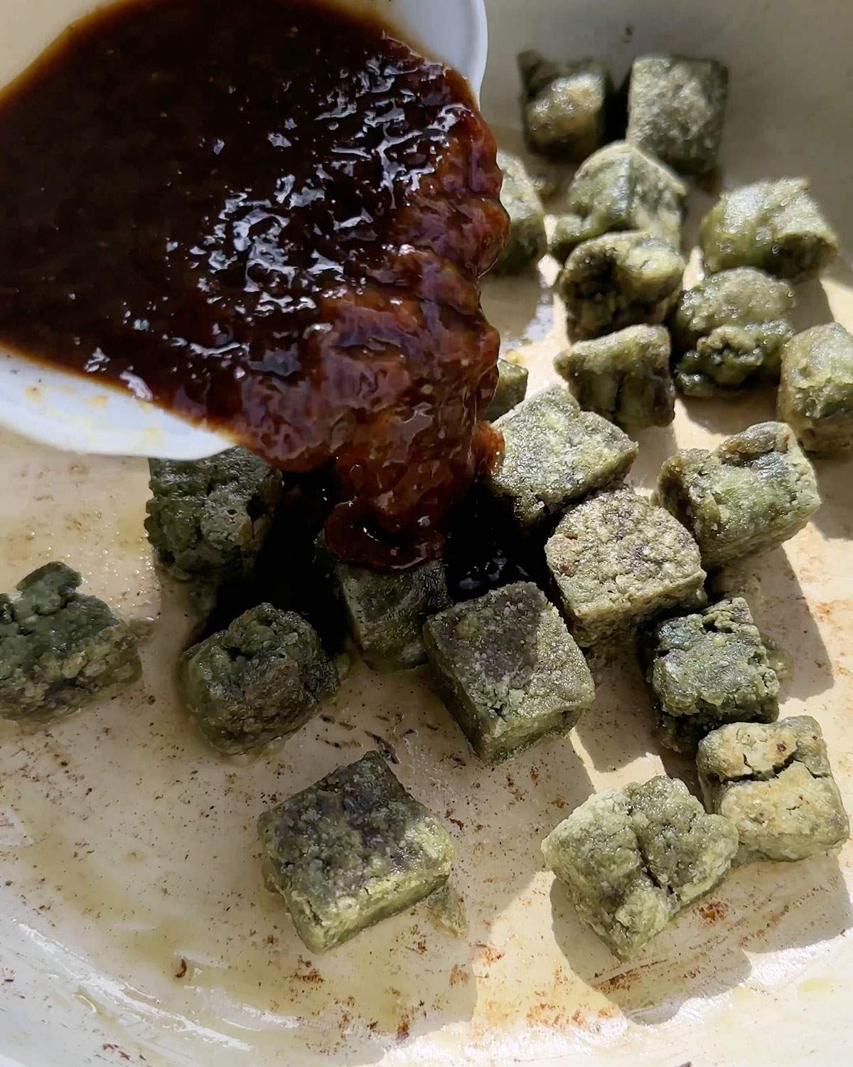 Pouring black pepper sauce into pumfu tofu cubes.
