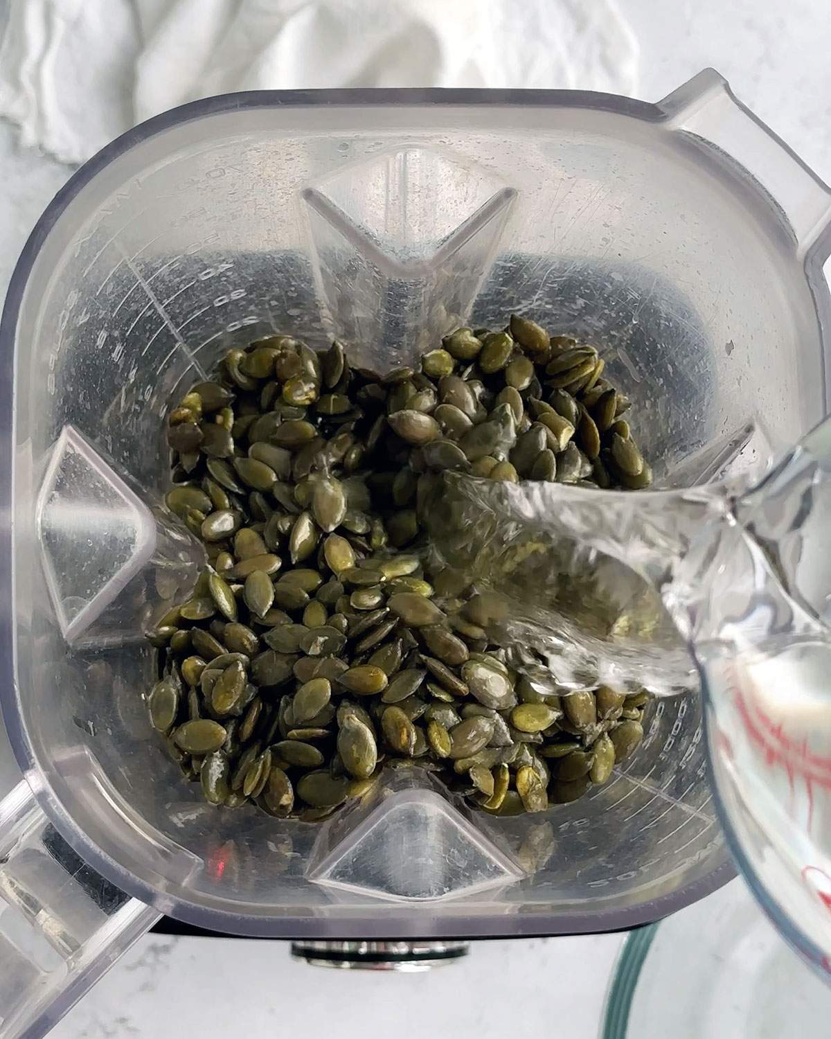 Pouring water onto pumpkin seeds in a blender.