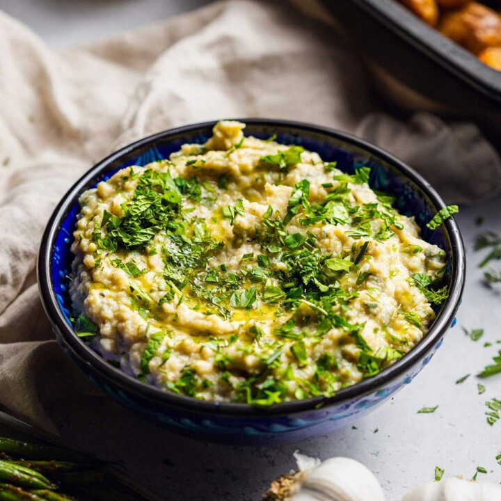 A bowl filled with herb butter bean mash with fresh herbs on top.