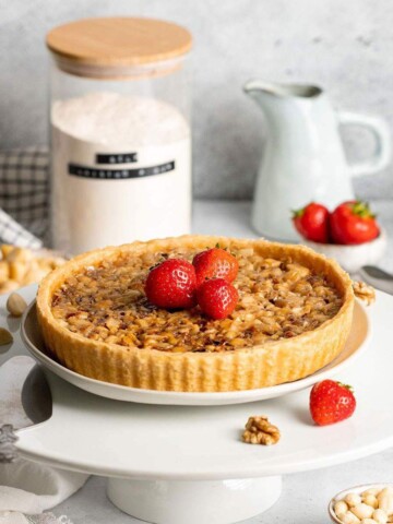 A vegan caramel tart on a cake stand decorated with strawberries.