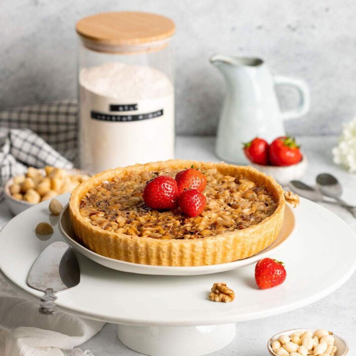 A vegan caramel tart on a cake stand decorated with strawberries.