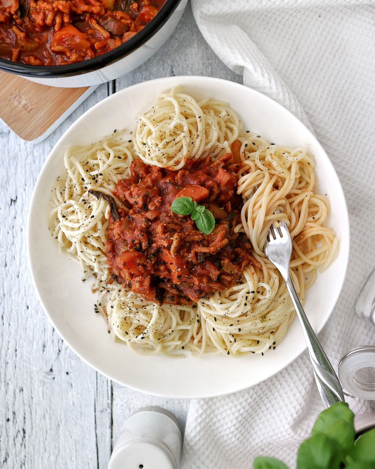 A plate with vegan spaghetti bolognese and a fork on the side.
