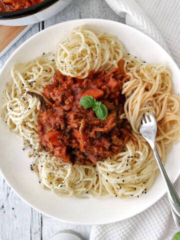 A plate with vegan spaghetti bolognese and a fork on the side.