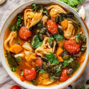 A bowl of vegan tortellini soup with fresh parsley on top.